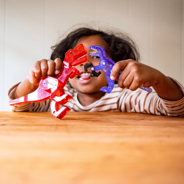 Young boy playing with red T-Rex and purple Velociraptor figurines from MAGNA-TILES® Dino World 40-Piece Set