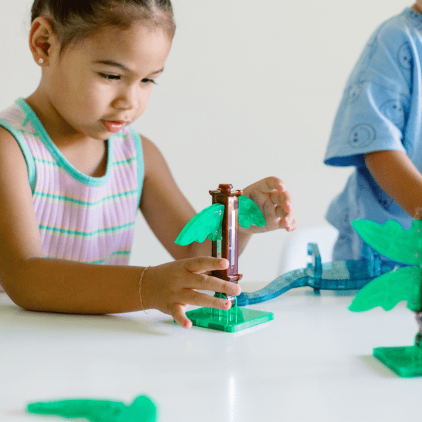 Young girl adding magnetic leaf to tree base from MAGNA-TILES® Dino World XL 50-Piece Set