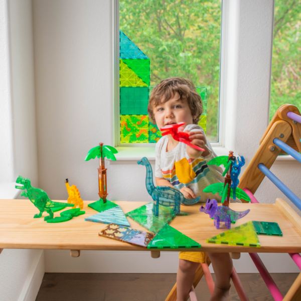 Young boy flies a red Pteranodon over his MAGNA-TILES® Dino World XL 50-Piece set