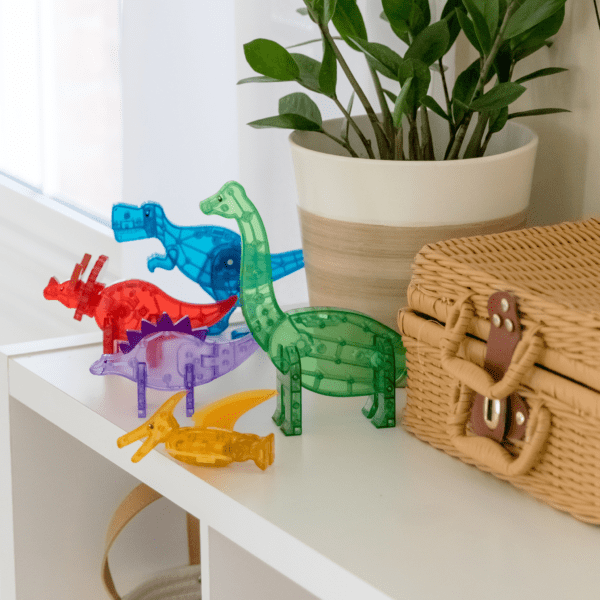 Blue T-Rex, green Brachiosaurus, red Triceratops, purple Stegosaurus, and yellow Pteranodon from MAGNA-TILES® Dinos 5-Piece Set sitting on a shelf.