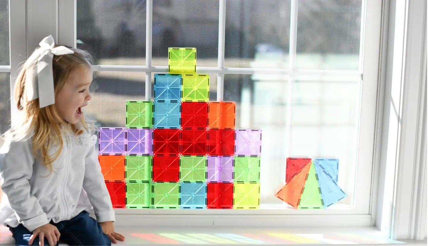 Happy, young girl sitting by a window with MAGNA-TILES®